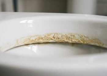 Depósito mineral amarelado acumulado na linha d'água de um vaso sanitário de porcelana