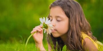 Criança deitada na grama cheirando flor descontraidamente