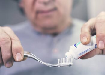 Homem aplicando creme dental em escova de dentes para escovação matinal