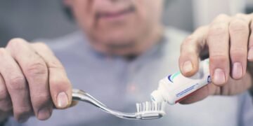 Homem aplicando creme dental em escova de dentes para escovação matinal