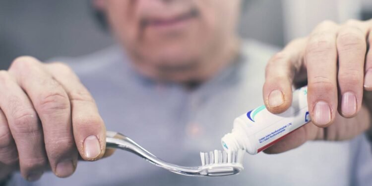 Homem aplicando creme dental em escova de dentes para escovação matinal
