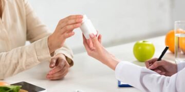 Médica prescrevendo e entregando cápsulas vitamínicas para paciente em consultório