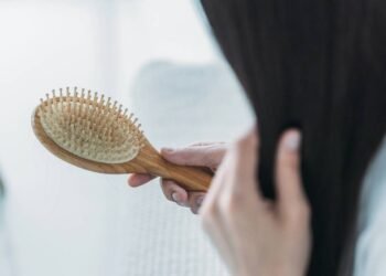 Mulher escovando o próprio cabelo enquanto observa na escova a sua queda de fios