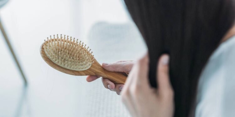 Mulher escovando o próprio cabelo enquanto observa na escova a sua queda de fios