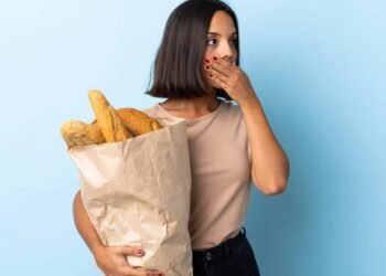 Mulher olhando para o lado em expressão de surpresa enquanto segura um saco com pães