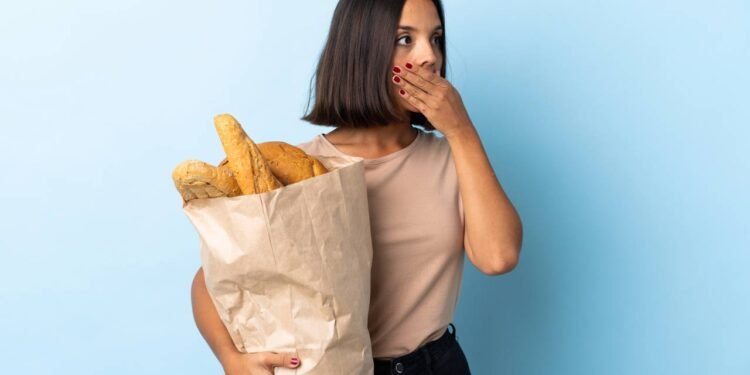 Mulher olhando para o lado em expressão de surpresa enquanto segura um saco com pães