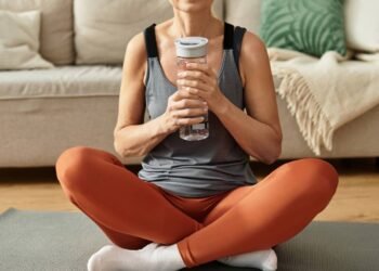 Mulher sentada em tapete de Yoga com garrafa cheia de água em mãos