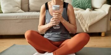 Mulher sentada em tapete de Yoga com garrafa cheia de água em mãos