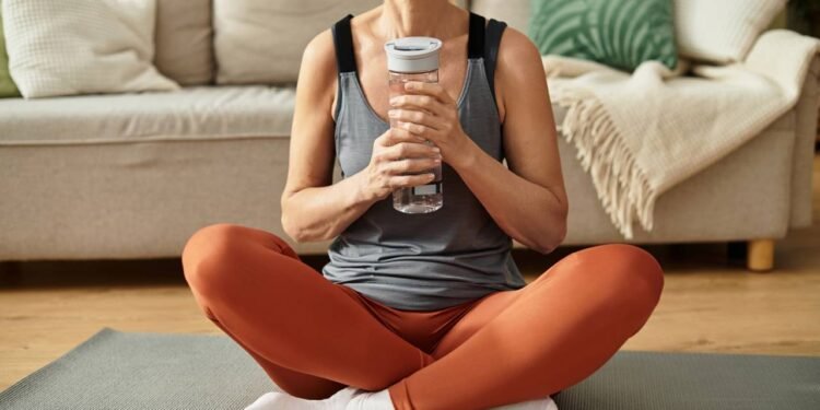Mulher sentada em tapete de Yoga com garrafa cheia de água em mãos