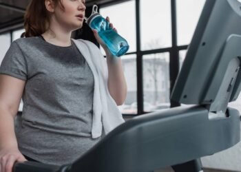 Mulher transpirando e se hidratando enquanto faz corrida em esteira ergométrica na academia