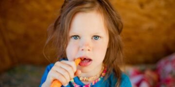 Pequena criança comendo uma cenoura