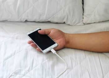 Pessoa segurando um celular carregando enquanto deita em cama