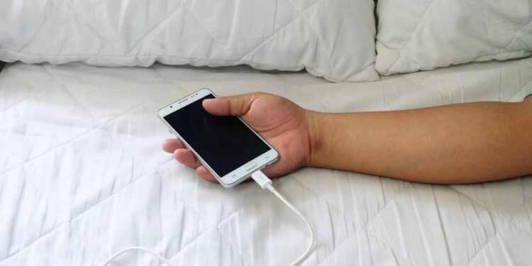 Pessoa segurando um celular carregando enquanto deita em cama