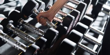Pessoa selecionando halteres para treinar na academia durante o dia