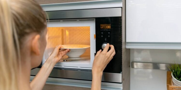 Pessoa usando microondas para aquecer alimentos na hora da refeição - Créditos: depositphotos.com / ronstik