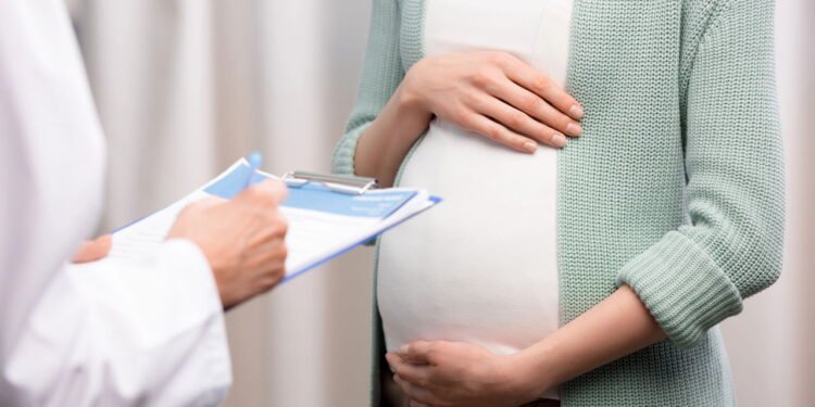 Médica com prancheta em frente a mulher grávida - Créditos: depositphotos.com / IgorTishenko