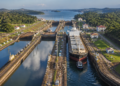 Vista aérea das eclusas do Canal do Panamá com um grande navio cargueiro sendo conduzido entre câmaras de concreto cercadas por vegetação.