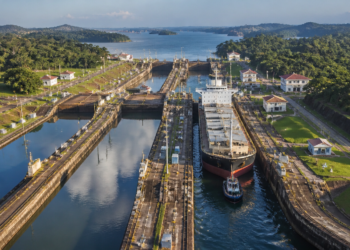 Vista aérea das eclusas do Canal do Panamá com um grande navio cargueiro sendo conduzido entre câmaras de concreto cercadas por vegetação.