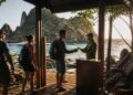 Visitantes com mochilas passam por um ponto de controle à beira-mar em Fernando de Noronha, onde um funcionário entrega um documento a um turista.
