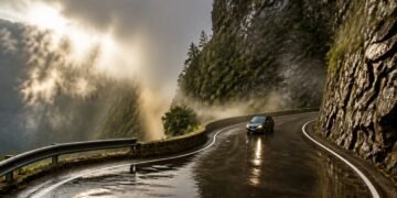 Carro percorre uma estrada sinuosa molhada na Serra do Rio do Rastro, entre paredões rochosos e neblina em meio à montanha.