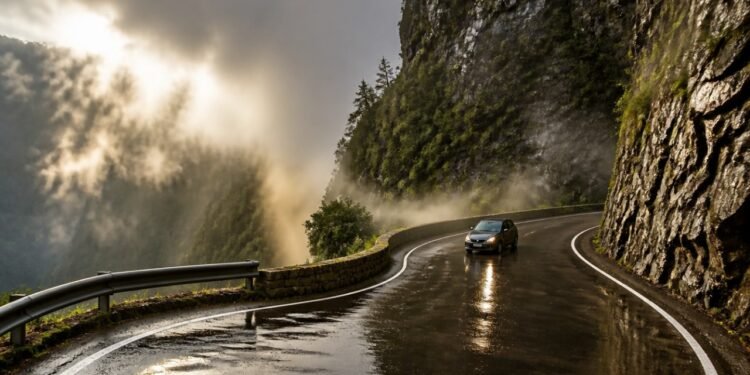 Carro percorre uma estrada sinuosa molhada na Serra do Rio do Rastro, entre paredões rochosos e neblina em meio à montanha.