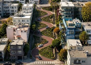 Vista aérea da Lombard Street em São Francisco, com carros percorrendo oito curvas fechadas entre jardins e edifícios residenciais.