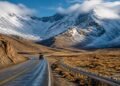 Estrada Ruta 40 atravessando uma paisagem árida dos Andes, com veículo, montanhas cobertas de neve e nuvens baixas.