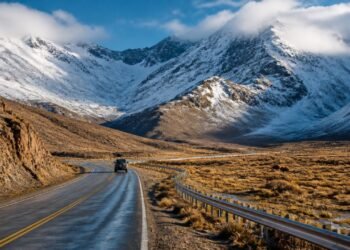 Estrada Ruta 40 atravessando uma paisagem árida dos Andes, com veículo, montanhas cobertas de neve e nuvens baixas.