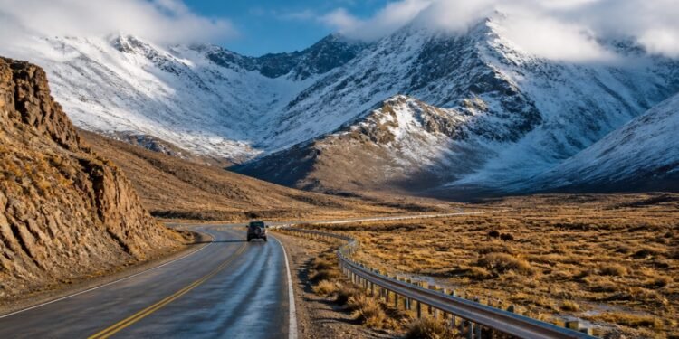 Estrada Ruta 40 atravessando uma paisagem árida dos Andes, com veículo, montanhas cobertas de neve e nuvens baixas.