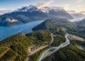 Vista aérea da Carretera Austral atravessando vales verdes da Patagônia chilena, ao lado de rios azul-turquesa, fiordes e montanhas nevadas.