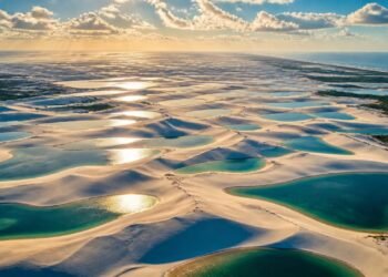 Vista aérea das dunas dos Lençóis Maranhenses com numerosas lagoas de água azul e verde formadas entre as faixas de areia clara.