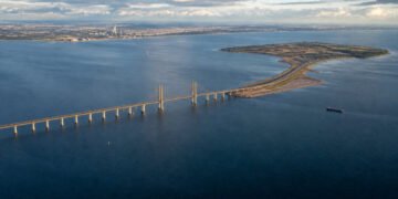 Vista aérea da Ponte de Øresund atravessando o mar até uma ilha artificial, com trecho estaiado, navio e áreas costeiras ao fundo.