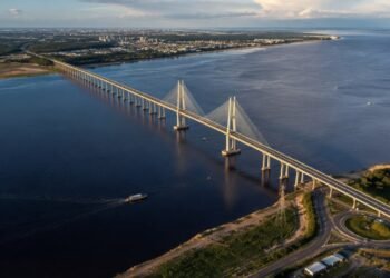 Vista aérea da Ponte Jornalista Phelippe Daou atravessando o rio Negro, com torres estaiadas, embarcações e áreas urbanizadas nas margens.