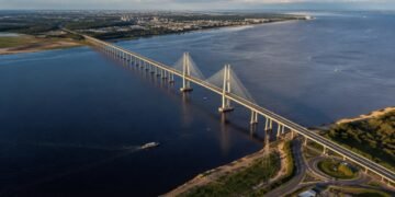 Vista aérea da Ponte Jornalista Phelippe Daou atravessando o rio Negro, com torres estaiadas, embarcações e áreas urbanizadas nas margens.