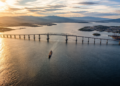 Vista aérea da Ponte Rio-Niterói atravessando a Baía de Guanabara ao pôr do sol, com um grande navio navegando sob o vão central.